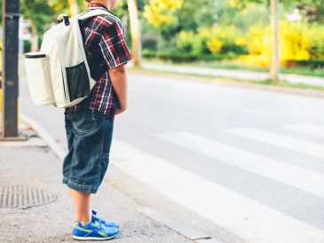 Child with a backpack waiting to cross the street at a crosswalk.