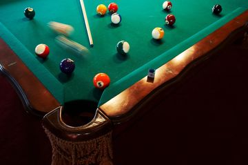 A lively moment in a billiards game with balls scattering near a pocket.
