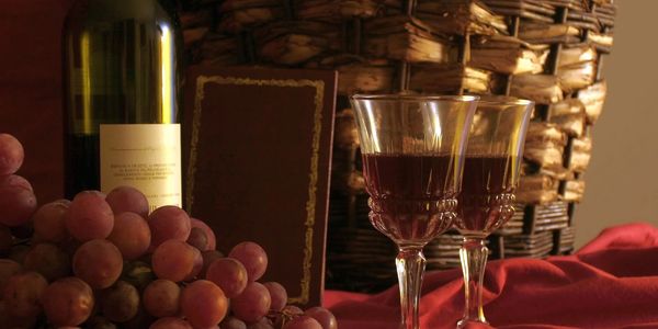 Wine bottle, grapes, and two filled wine glasses on a red cloth.