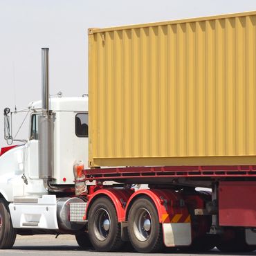 White semi-truck hauling a large yellow shipping container on a clear day.