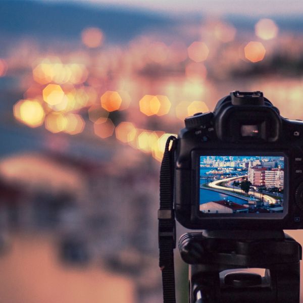 Camera capturing a cityscape with evening lights bokeh in the background.