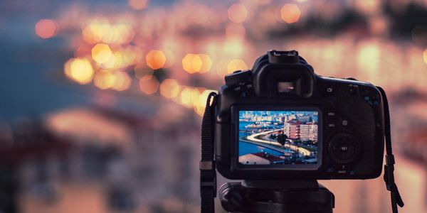 Digital camera on tripod, overlooking blurry cityscape in distance.