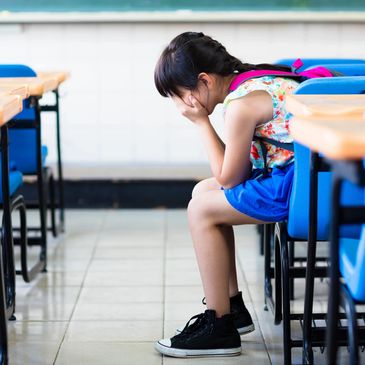 Girl in a classroom with her face in her hands.