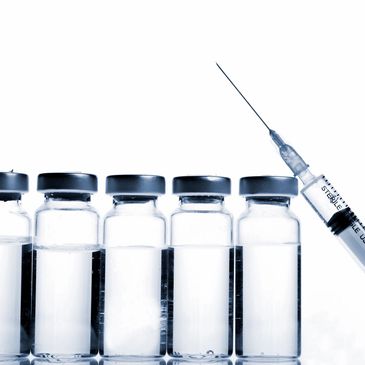 Row of vaccine vials with a syringe poised to inject.