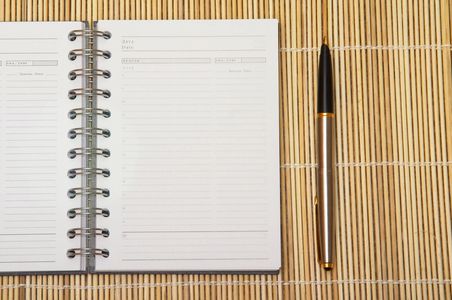Open spiral notebook and pen on bamboo mat.