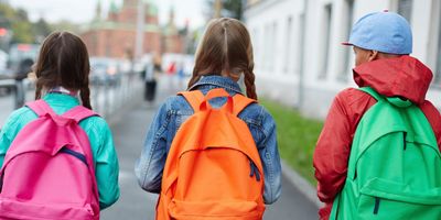 Three children walking with colorful backpacks on a city street.