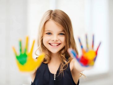 Smiling girl showing colorful painted hands to the camera.