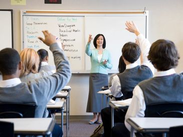 Teacher engaging students with raised hands in classroom discussion.