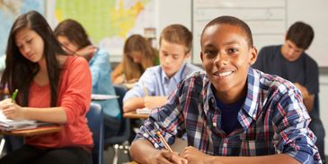 Smiling student in a classroom with peers focused on their work.