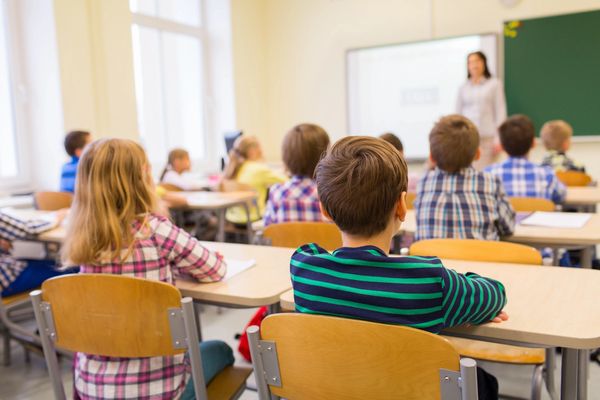 Children attentively listening to a teacher in a classroom setting.
