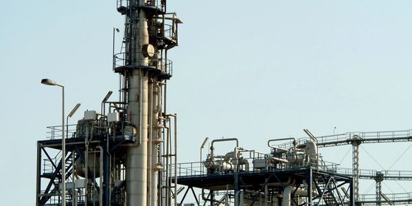 Industrial refinery tower with pipes and platforms against a clear sky.