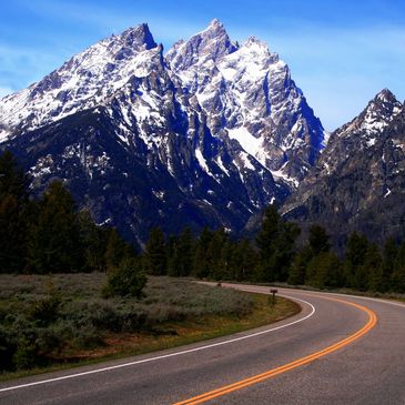 Curving road leading to snow-capped mountain peaks under clear blue sky.