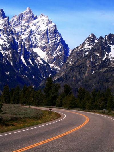 Curved road leading to snow-capped mountain peaks under a clear blue sky.