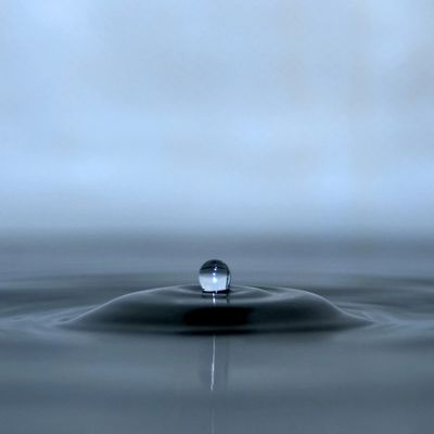 A water droplet suspended above a calm surface creating ripples.
