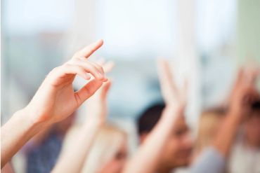 Several hands raised in a classroom or meeting setting.