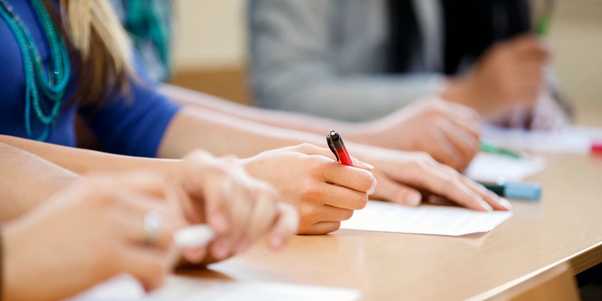 People writing on papers at a desk with pens.