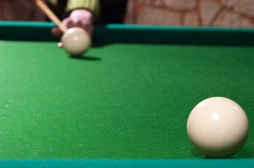 A close-up of a billiard ball on a pool table with a player aiming in the background.