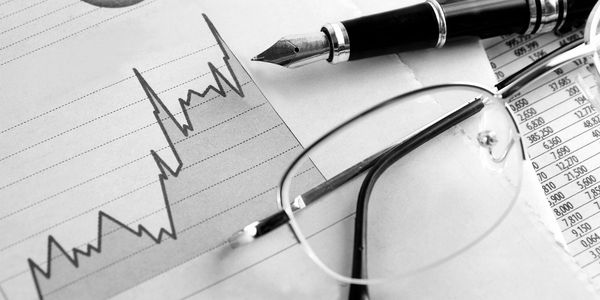 Fountain pen and glasses on a financial graph and data sheets.