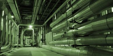 Industrial hallway lined with large metal pipes and machinery under green lighting.