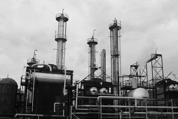 Black and white photo of an industrial refinery with tall chimneys and pipes.