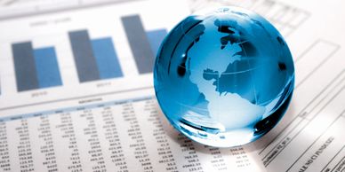 Stock photo of blue clear glass round world globe sitting on top of paper that includes bar graphs 