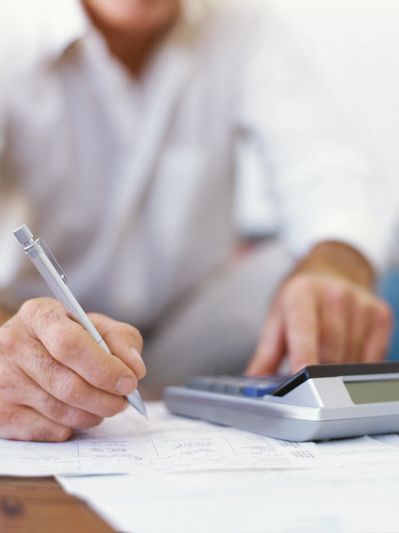 Person calculating finances using a calculator and writing notes.