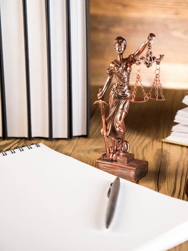 Justice statue with a pen and notebook on a wooden table.