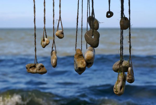 Stones tied with strings hanging over water.