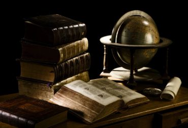 Old books and a globe on a wooden table.