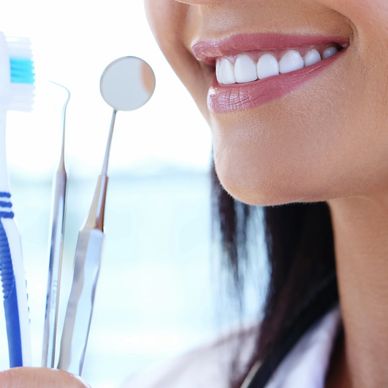 Close-up of a smiling woman holding dental tools and a toothbrush.