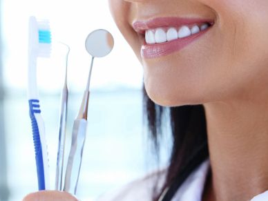 Close-up of a smiling woman holding dental tools and a toothbrush.