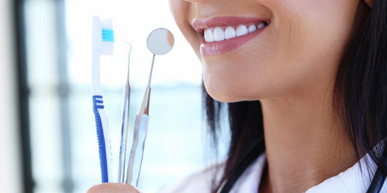 Dental professional holding a mirror and tooth brush, she has a very pretty smile and dark hair