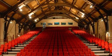 Empty auditorium with red seats and wooden ceiling beams.