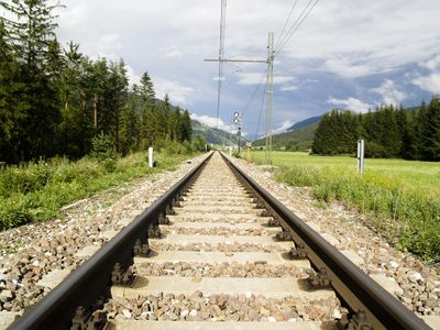 Railway tracks stretching into a scenic countryside landscape under a partly cloudy sky.