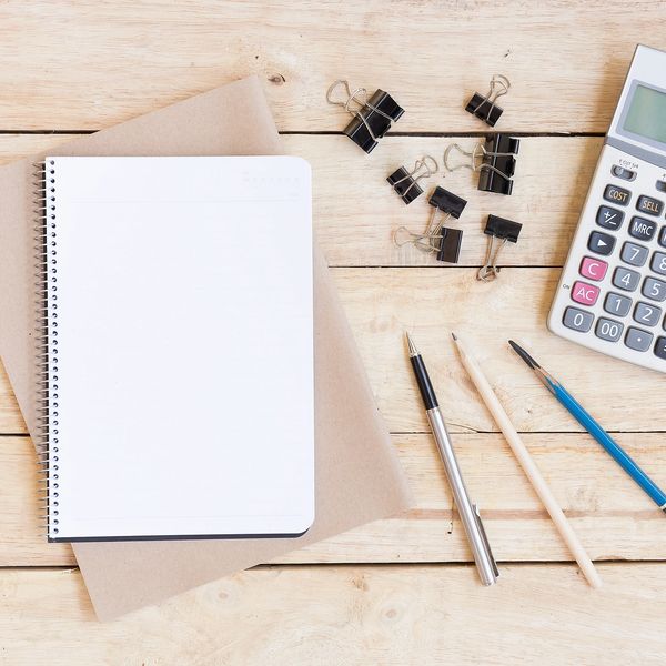 A workspace with a blank notebook, pens, clips, and a calculator on a wooden surface.