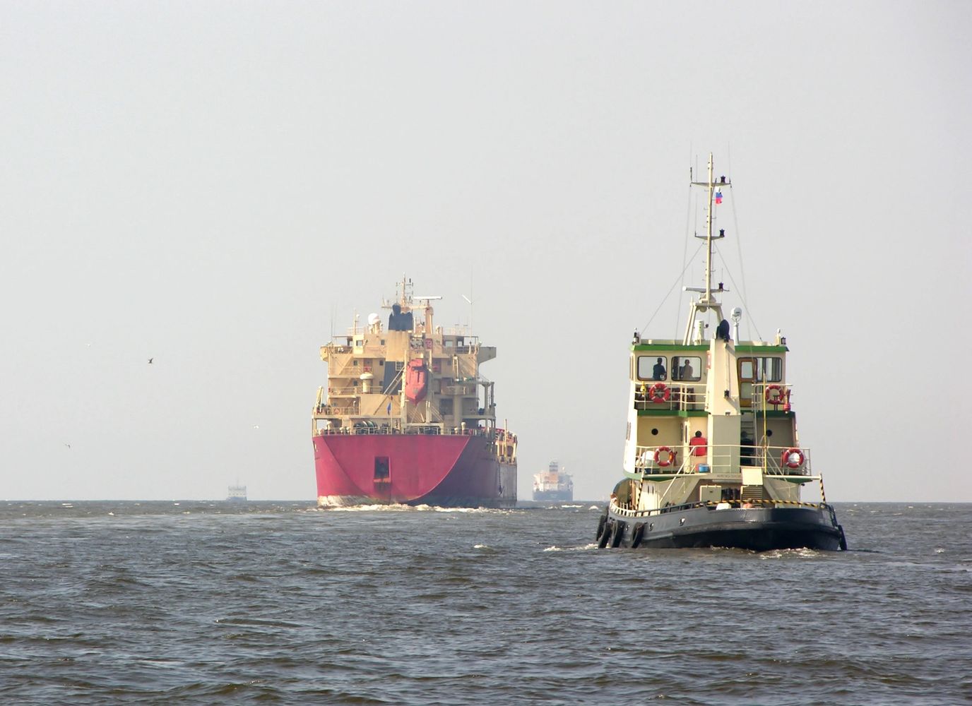A tugboat guiding large cargo ships on a calm sea under a clear sky.
