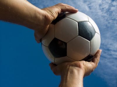 Hands holding a classic black and white soccer ball against a blue sky.