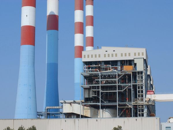 Industrial building with tall, striped chimneys against a clear blue sky.
