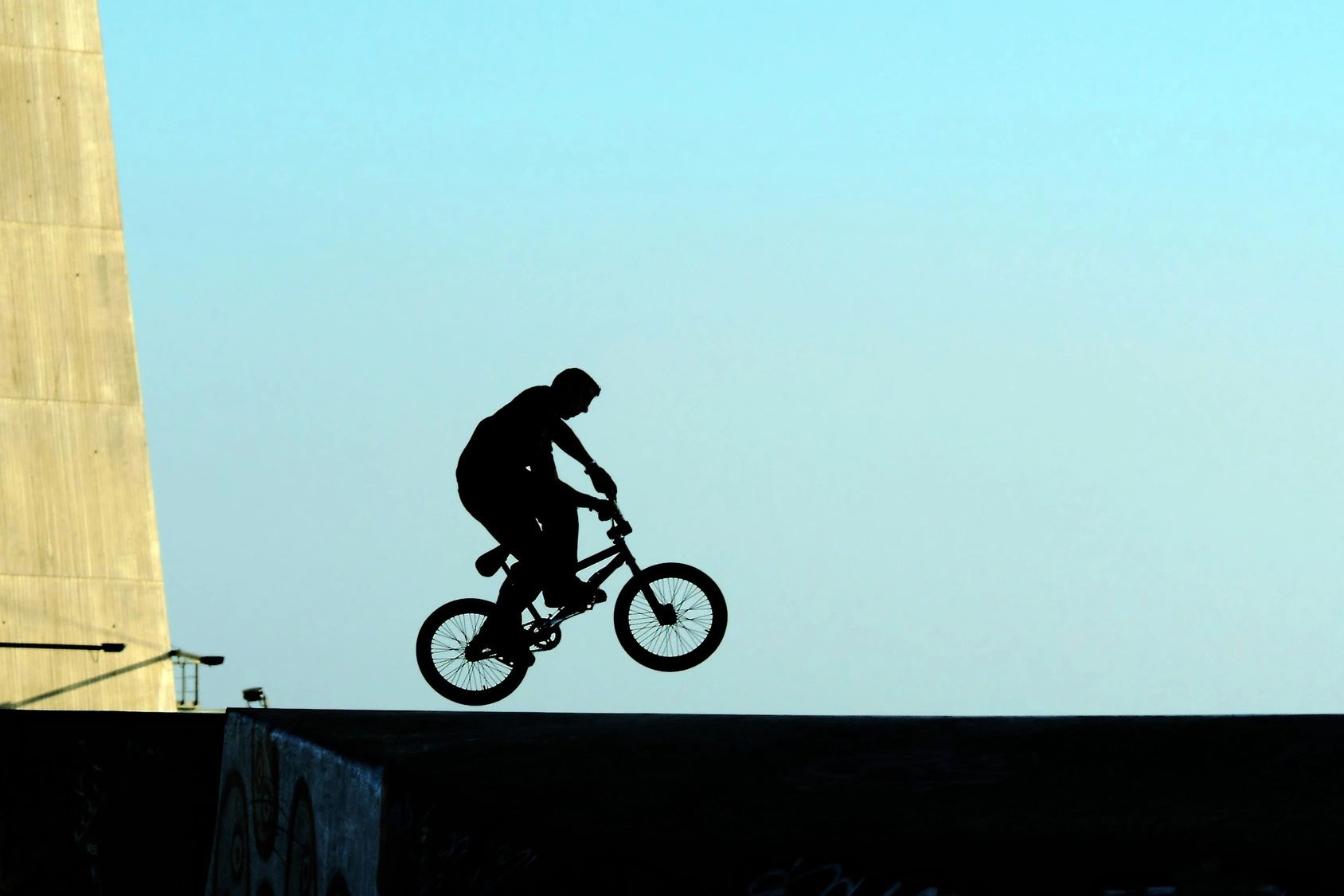Silhouette of a person performing a bike stunt against a clear sky.