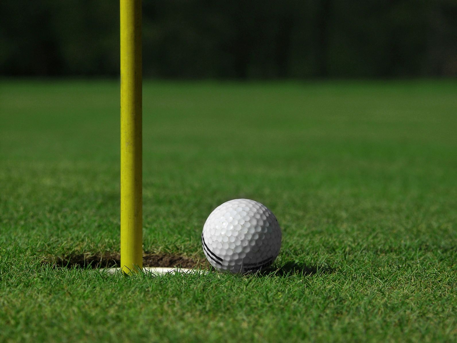 Golf ball near hole on a green with yellow flagstick.