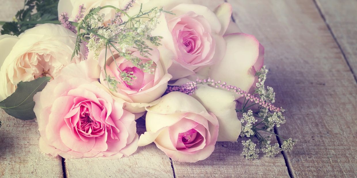Soft pink and white roses with delicate greenery on rustic wood.