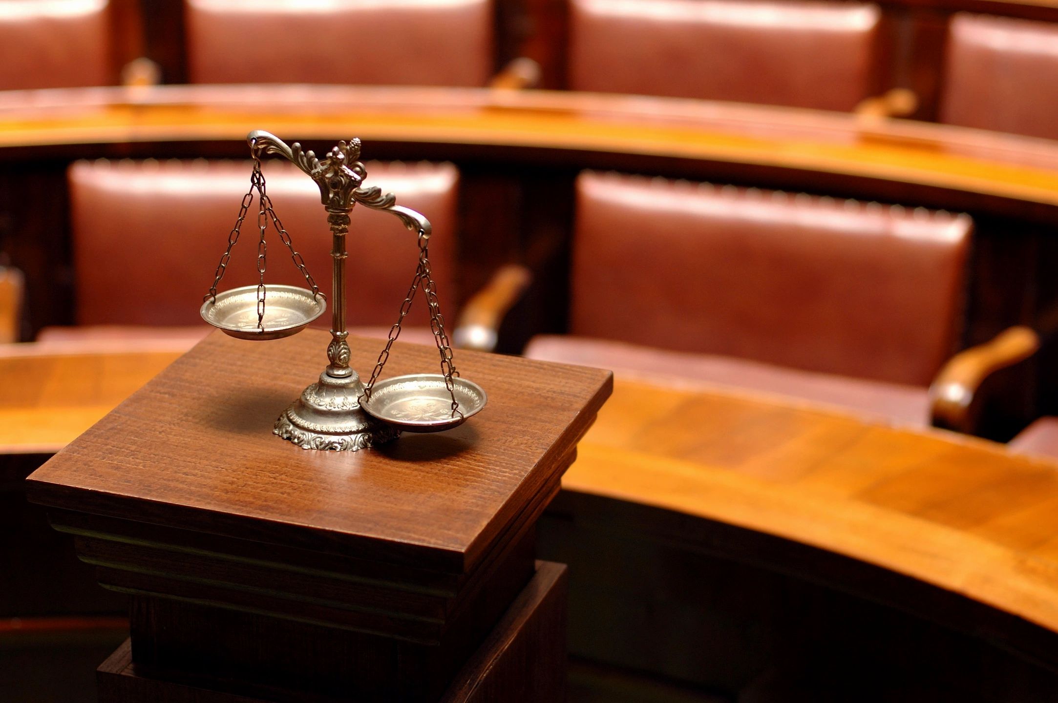 A scale of justice sits on a wooden podium in a courtroom