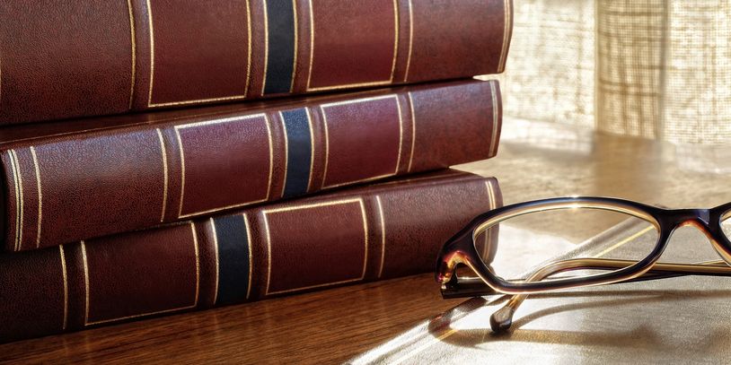 Stack of leather-bound books with eyeglasses on wooden table.