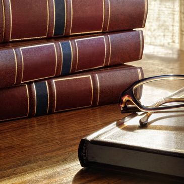 Glasses sitting on top of a book with three large books sitting next to them on a desk.