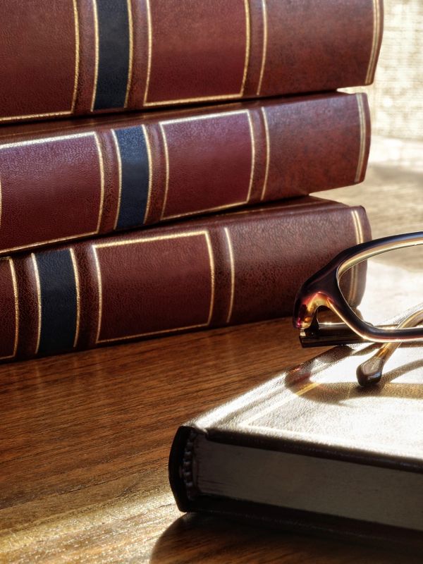 Stack of vintage books and reading glasses on a wooden table.