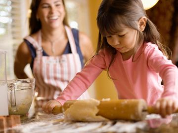 Young girl and mother rolling dough in the kitchen