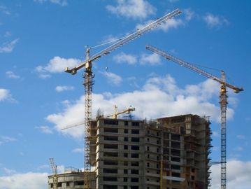 Construction cranes working on a high-rise building under a blue sky.