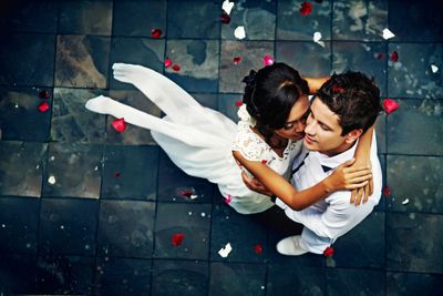Bride and groom embracing on a tiled floor scattered with rose petals.