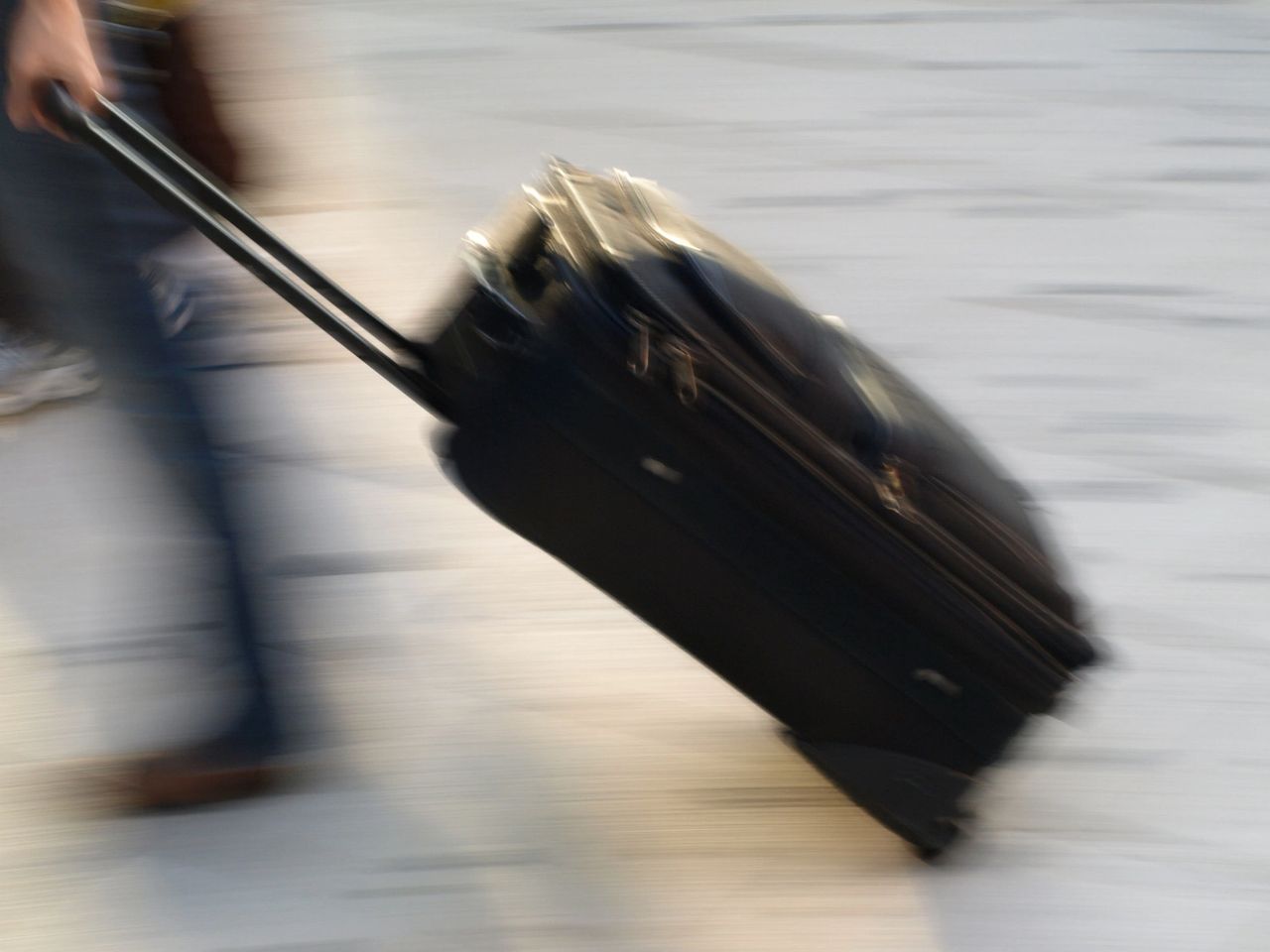 View of a person in-motion as they pull their wheeled suitcase behind them.