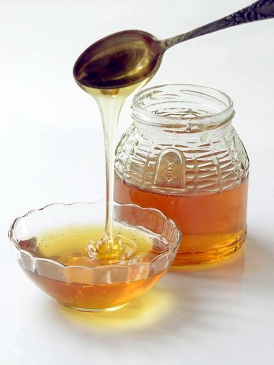 Honey being poured from a spoon into a glass bowl beside a jar.